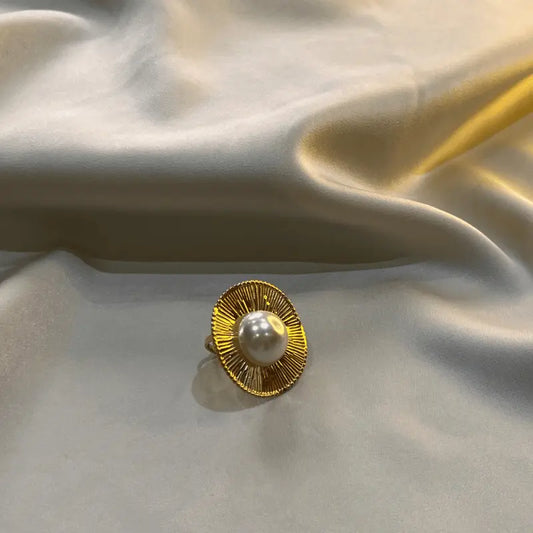 Bague en acier inoxydable dorée avec une perle, posée sur un fond en tissu brillant