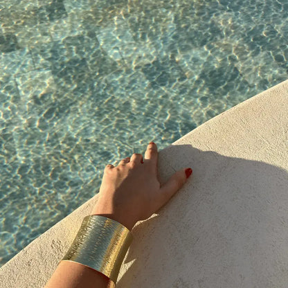 Bracelet manchette en acier inoxydable porté près de l'eau, mettant en valeur sa texture dorée brillante en plein soleil.
